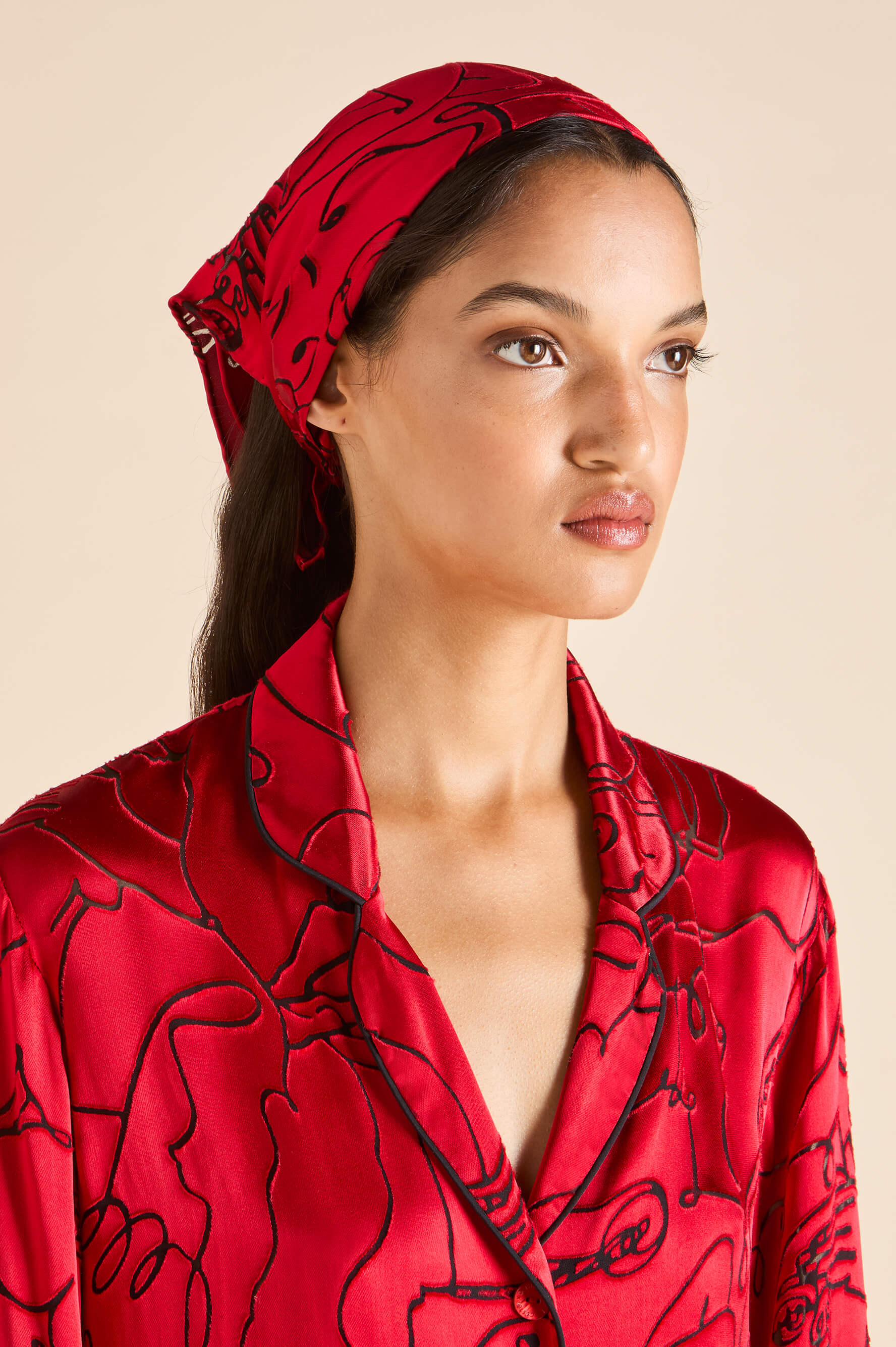 olivia von halle red silk scarf with black figure detail styled on a model's hair 